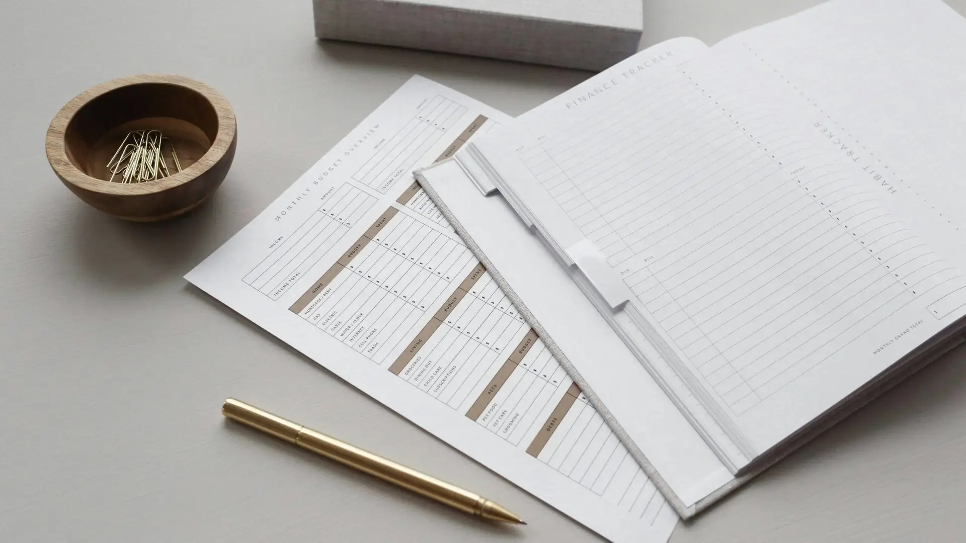 Financial planning documents with a gold pen and a bowl of paper clips on a table.