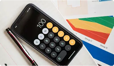 A smartphone with a calculator app showing "100", placed on a notebook with financial charts and a pen.